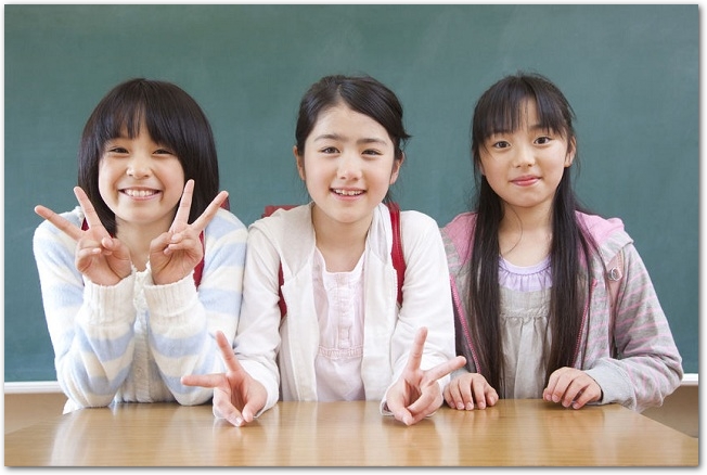 教室の黒板の前に立つ笑顔の女子小学生３人